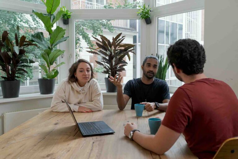 Three people discussing at table with laptop